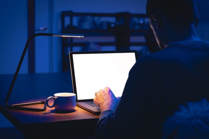 A man works in a dark room, uses a laptop at night.