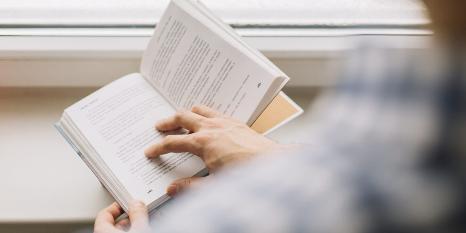 crop-man-reading-book-near-window